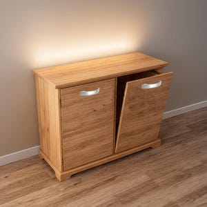 Puede incluir: Un mueble de madera clara con dos puertas, una ligeramente entreabierta. La madera muestra vetas visibles. Cada puerta tiene un tirador plateado. El mueble está sobre un suelo de madera.