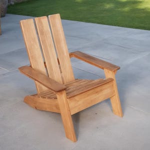 May include: A wooden Adirondack chair with a natural finish. The chair features a slatted seat, wide armrests, and a tall back with vertical slats. It is designed for outdoor use and is placed on a concrete patio.