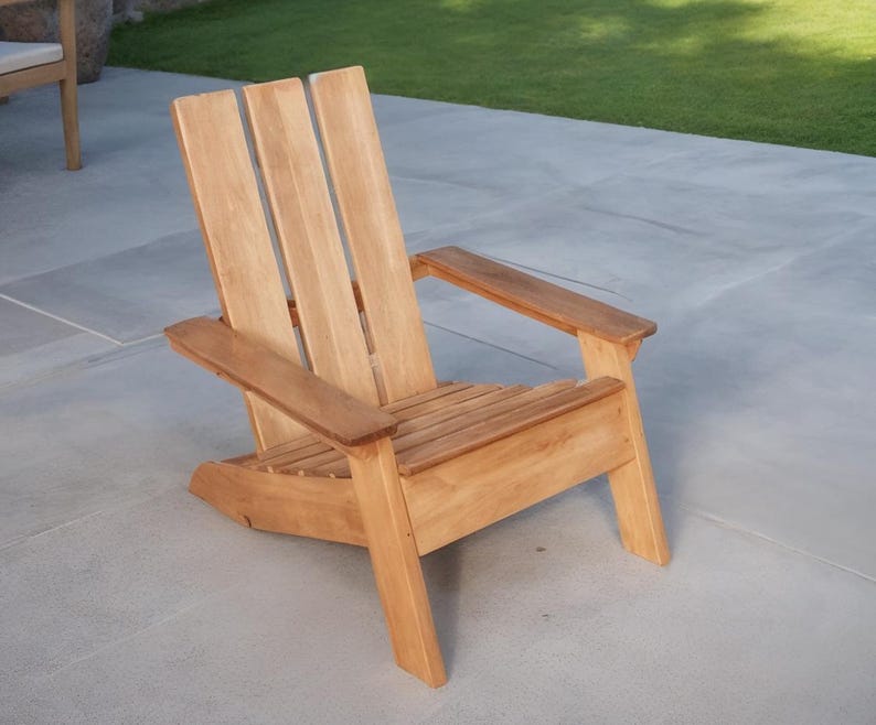 May include: A wooden Adirondack chair with a natural finish. The chair features a slatted seat, wide armrests, and a tall back with vertical slats. It is designed for outdoor use and is placed on a concrete patio.