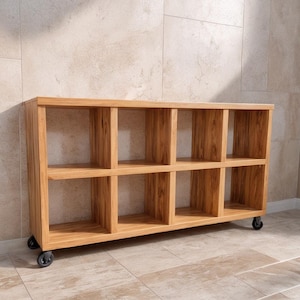 May include: A light brown wooden storage unit with ten cubby holes. The unit is rectangular and sits on four small black wheels. The wood grain is visible. The unit is against a light beige tiled wall.