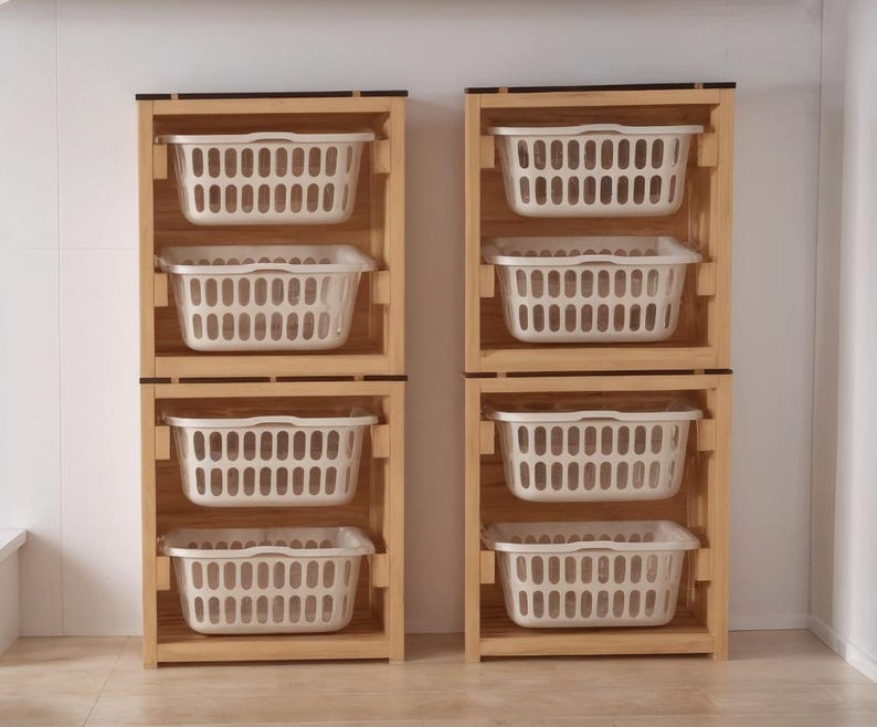 May include: Two wooden laundry sorters, each with three white plastic baskets. The sorters are made of light-colored wood and have a simple, rectangular design. The baskets are rectangular with a slotted design.