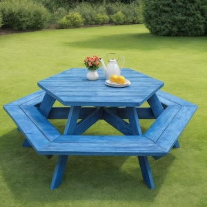 Könnte beinhalten: Blauer Picknicktisch aus Holz mit achteckiger Tischplatte und angebrachten Bänken. Eine weiße Teekanne, eine kleine Vase mit Blumen und ein Teller mit Zitronen stehen auf dem Tisch. Der Tisch steht im Freien auf einer grünen Wiese.