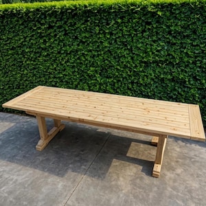 Könnte beinhalten: Ein großer, rechteckiger Holztisch mit natürlicher Oberfläche. Der Tisch hat eine Lattenoberfläche und abgewinkelte Beine. Der Tisch ist ca. 244 cm lang und 102 cm breit, geeignet für Mahlzeiten im Freien.