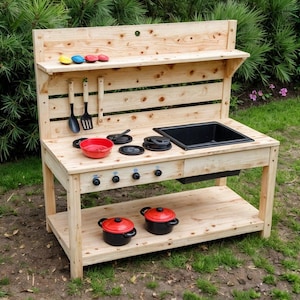 May include: A wooden outdoor play kitchen with a black sink, stove top, and shelf. It includes a red pot, black utensils, and colorful play food. The kitchen is made of light-colored wood and is designed for children.
