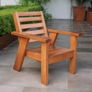 May include: A wooden outdoor chair with a natural finish. The chair has a slatted back and seat, with armrests. The chair is made of solid wood and is designed for outdoor use. The chair is approximately 24 inches wide, 24 inches deep, and 30 inches tall.
