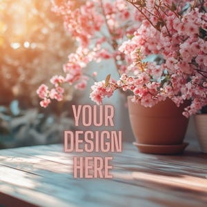 May include: A wooden table with the text "YOUR DESIGN HERE" in pink letters. The table is in front of a window with plants and pink flowering branches in pots and vases. The Siren Vault Design Studio logo is in the bottom right corner.