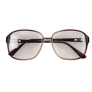 May include: Eyeglasses featuring a gradient frame that transitions from a dark brown at the outer edges to a lighter, translucent amber tone toward the center bridge. The clear lenses are set within an oval-shaped frame with 52/18 140 printed on the inner arm.