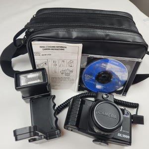 May include: A black 35mm DL1000 camera with a flash, instruction manual, and a Canon CD. The camera has a lens cap that says "CAMERA". The set includes a black camera bag with a shoulder strap.