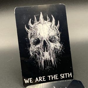 May include: Black card with a white illustration of a horned skull. The text "WE ARE THE SITH" is printed in white at the bottom. The card has rounded corners and a glossy finish. A second card is partially visible.
