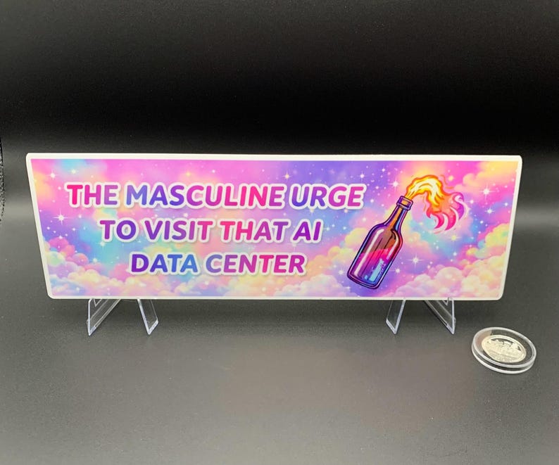 Peut inclure: Panneau rectangulaire avec le texte "THE MASCULINE URGE TO VISIT THAT AI DATA CENTER" et une illustration d'une bouteille avec des flammes. Le panneau est soutenu par des supports en plastique transparents et une pi&egrave;ce de monnaie est visible.
