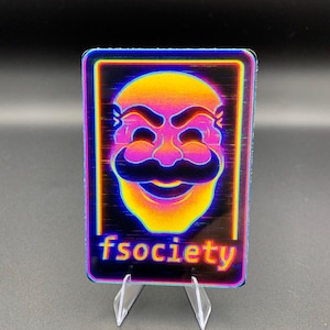 Peut inclure: Une carte rectangulaire avec un masque stylisé et une moustache dans des tons de jaune, orange et rose, avec un effet de glitch. Le texte "fsociety" est en bas. La carte est présentée sur un présentoir en acrylique transparent.