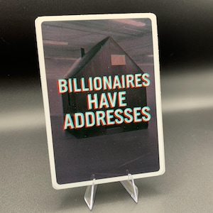 Könnte beinhalten: Eine rechteckige Karte mit dem Text "BILLIONAIRES HAVE ADDRESSES" in 3D-Effekt. Das Bild auf der Karte zeigt eine dunkle Haussilhouette. Die Karte wird auf einem transparenten Kunststoffständer vor dunklem Hintergrund präsentiert.