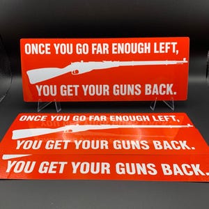 May include: A rectangular red sign featuring white text that reads ONCE YOU GO FAR ENOUGH LEFT, YOU GET YOUR GUNS BACK. A white silhouette of a rifle is positioned horizontally between the two lines of text on the sign.