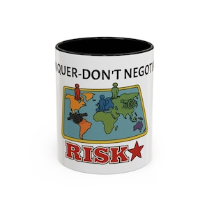 Op de afbeelding: Witte keramische mok met een zwarte binnenkant met een kleurrijk wereldkaartontwerp. De kaart toont continenten met figuren en kanonnen, en het woord "RISK" in rood met een ster. De mok heeft ook de tekst "CONQUER-DON'T NEGOTIATE".