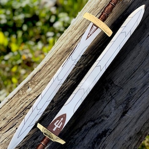 May include: Two decorative swords with white blades and brown handles are displayed on a wooden surface. The swords have gold-colored crossguards and pommels. One sword has a trident symbol on the blade.
