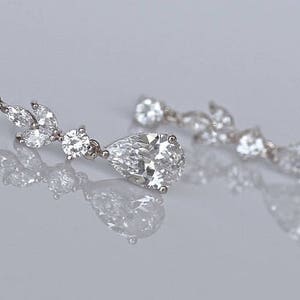 May include: A pair of silver dangle earrings with pear-shaped and round clear crystals.