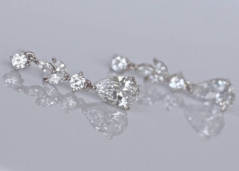 May include: A pair of silver dangle earrings with pear-shaped and round clear crystals.