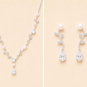 May include: A silver-toned necklace and matching earrings set. The necklace features a vine-like design with clear crystals, pearls, and a pear-shaped pendant. The earrings have a pearl top, a vine design, and a pear-shaped crystal.