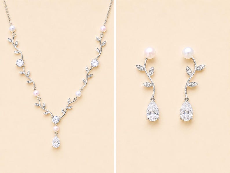May include: A silver-toned necklace and matching earrings set. The necklace features a vine-like design with clear crystals, pearls, and a pear-shaped pendant. The earrings have a pearl top, a vine design, and a pear-shaped crystal.