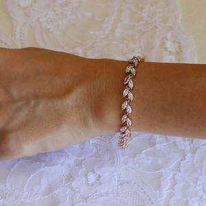 May include: A rose gold bracelet with a delicate chain and marquise-shaped clear stones. The stones are set in a leaf-like pattern.