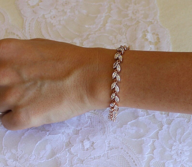 May include: A rose gold bracelet with a delicate chain and marquise-shaped clear stones. The stones are set in a leaf-like pattern.