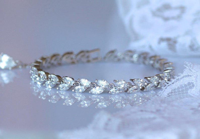 May include: A silver bracelet with a row of marquise-shaped clear stones set in a leaf design.