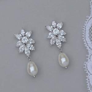 K&ouml;nnte beinhalten: Ein Paar silberne Ohrringe mit einem floralen Design und einem Perlenanh&auml;nger. Die Ohrringe sind aus klaren Zirkonia-Steinen gefertigt.