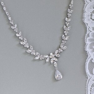 May include: A silver necklace with a teardrop pendant and a delicate design of clear crystals arranged in a leaf pattern.