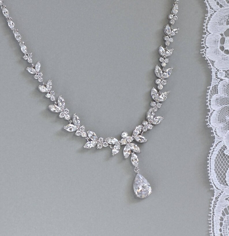 May include: A silver necklace with a teardrop pendant and a delicate design of clear crystals arranged in a leaf pattern.