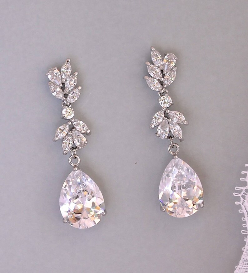 May include: A pair of silver teardrop earrings with clear crystal accents. The earrings feature a cluster of smaller crystals at the top and a larger teardrop-shaped crystal at the bottom.