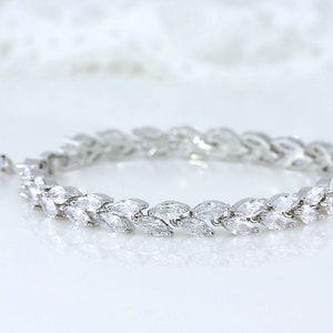 May include: A silver bracelet with a delicate design of marquise-shaped stones set in a row. The bracelet is made of metal and has a polished finish.