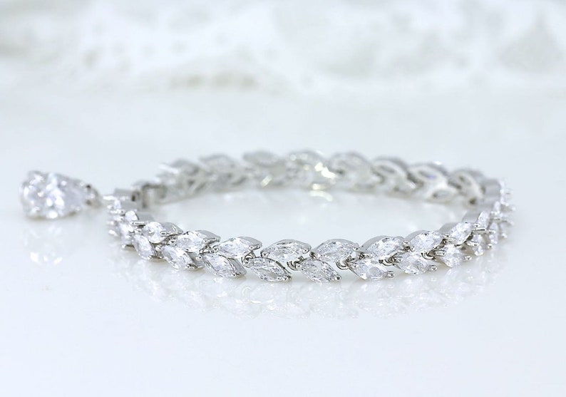 May include: A silver bracelet with a delicate design of marquise-shaped stones set in a row. The bracelet is made of metal and has a polished finish.