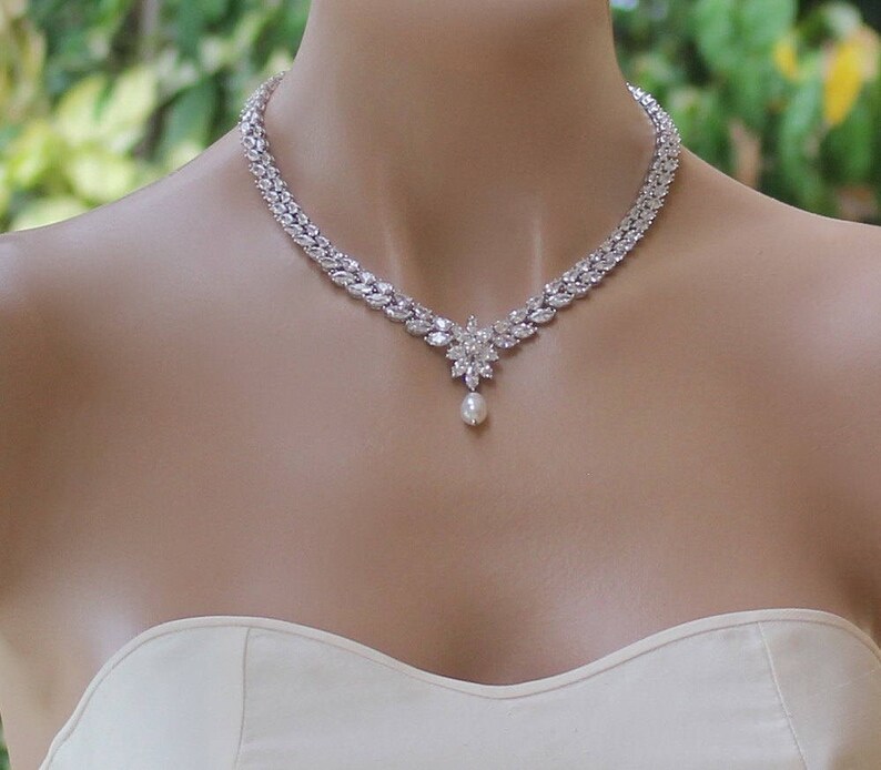 K&ouml;nnte beinhalten: Eine silberne Halskette mit einem perlmuttfarbenen Anh&auml;nger und einem floralen Design. Die Halskette besteht aus kubischen Zirkonia-Steinen und ist perfekt f&uuml;r eine Hochzeit oder einen besonderen Anlass.