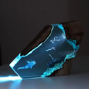 May include: A resin sculpture of a blue whale and other sea life, set in a wooden base. The resin is clear and glows blue, creating a luminous effect.