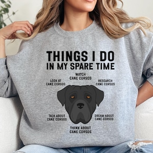 May include: A grey sweatshirt featuring the text "THINGS I DO IN MY SPARE TIME" and a Cane Corso dog graphic. The design includes phrases such as "Watch Cane Corsos" and "Think about Cane Corsos."