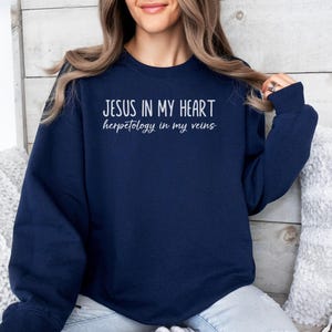 以下が含まれることがあります： 「JESUS IN MY HEART」の白文字と「herpetology in my veins」がプリントされたネイビーブルーのスウェットシャツ。長袖で無地なので、カジュアルウェアに適しています。