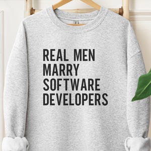 Grey sweatshirt with black text that reads "REAL MEN MARRY SOFTWARE DEVELOPERS".