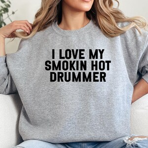 Può includere: Felpa grigio chiaro con la scritta nera "I LOVE MY SMOKIN HOT DRUMMER". Il top a maniche lunghe ha uno scollo tondo ed è realizzato in materiale morbido.