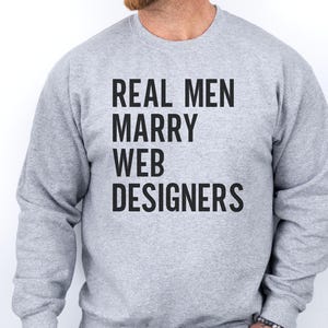 Può includere: Una felpa grigio chiaro a girocollo con il testo nero "REAL MEN MARRY WEB DESIGNERS" stampato in un carattere grassetto senza grazie al centro del petto. Il capo presenta maniche lunghe e bordi a costine su colletto, polsini e orlo.