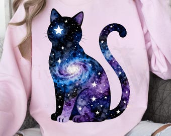 May include: A light pink sweatshirt featuring a black cat silhouette filled with a galaxy design. The galaxy design includes swirls of blue, purple, and white stars. A large white star is in the cat's eye.