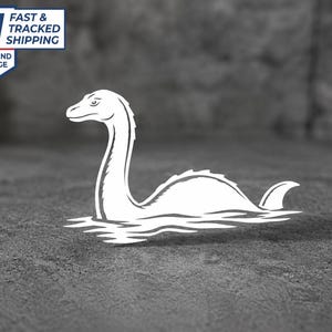 May include: A white vinyl decal featuring a stylized graphic of the Loch Ness Monster with a long neck and humped back emerging from water. The design is solid white with clean lines, depicting the creature in profile facing to the left.
