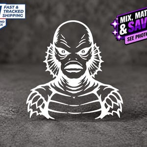 May include: A white vinyl decal featuring a stylized graphic illustration of the Creature from the Black Lagoon. The design depicts the creature's head, neck, and upper torso with detailed scales, fins, and facial features in a high-contrast silhouette.