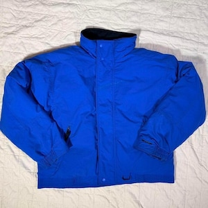 May include: A vibrant blue jacket with a high collar and a black interior lining. The jacket features a zipper closure, button details, and elastic cuffs. This outerwear garment is designed for warmth and protection from the elements.
