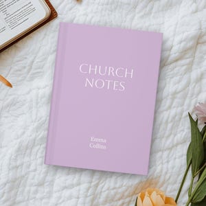 Könnte beinhalten: Ein lavendelfarbenes Notizbuch mit dem weißen Schriftzug "CHURCH NOTES". Der Name "Emma Collins" ist darunter aufgedruckt. Das Notizbuch liegt auf einer weißen, strukturierten Oberfläche, mit einer Bibel und Blumen im Hintergrund.