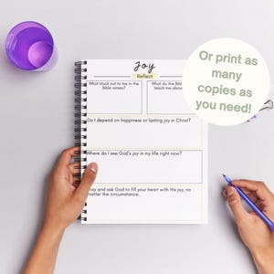 May include: A spiral-bound journal with the word "Joy" at the top, featuring prompts for reflection. The journal includes sections for Bible verses, teachings, and personal experiences. A purple cup and a pen are also visible.