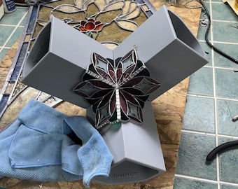 May include: A gray, three-sided display stand with a stained glass butterfly decoration. The butterfly features burgundy, green, and clear glass pieces. A blue microfiber cloth rests on the wooden work surface.