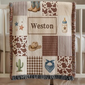 May include: A woven throw blanket featuring a patchwork design with brown and white cow print, brown stripes, and brown gingham patterns. Illustrations include cowboy boots, a hat, a cactus, a baby bottle, and stars. The name Weston is printed in the center.