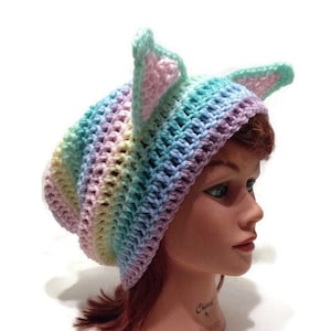 May include: A rainbow colored crochet hat with cat ears. The hat is made with a variety of pastel colors, including pink, blue, green, and yellow.