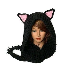 May include: Black hooded scarf with pink cat ears and a long tail. The scarf is crocheted and has a fringe at the end of the tail.