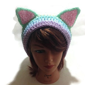 May include: A crocheted hat with cat ears in shades of purple, blue, green, and pink. The hat is on a mannequin head.